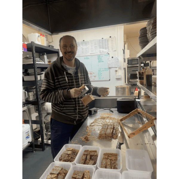 Laszlo from BeesFriend cutting fresh honeycomb into portions in a commercial kitchen, with packed comb sections ready for sale