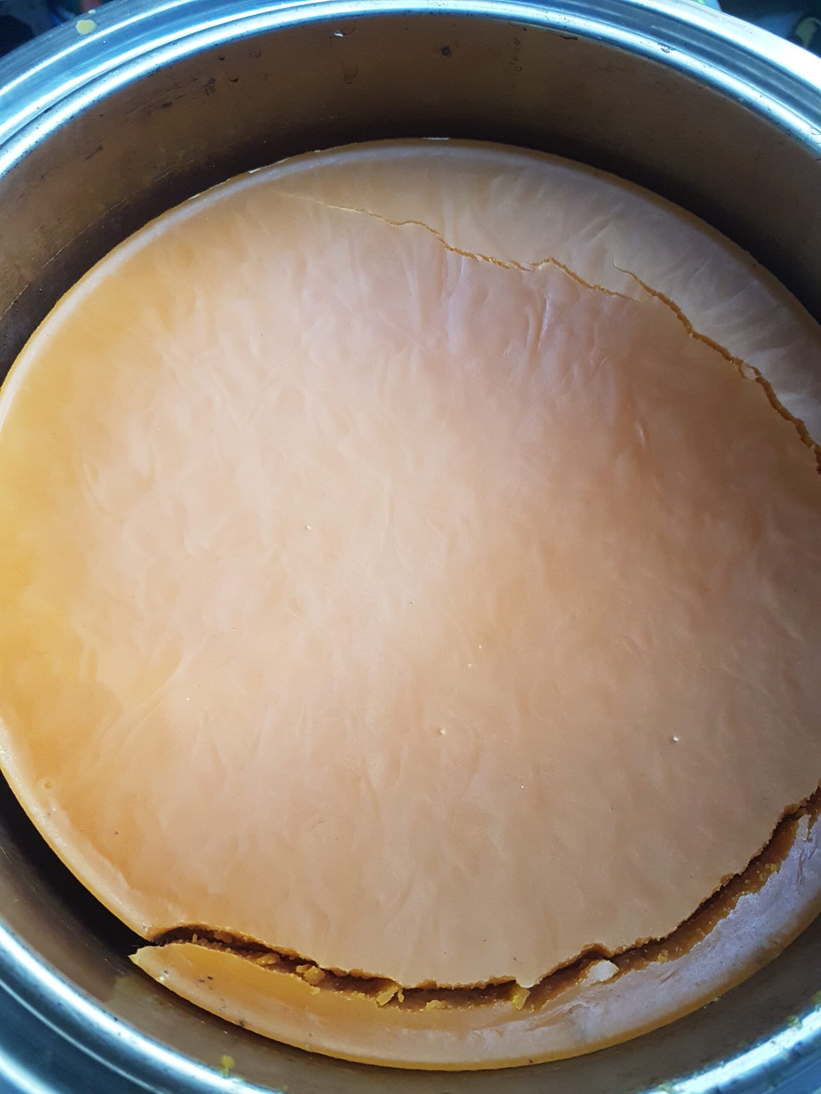 A clean round of rendered golden beeswax set in a stainless pot
