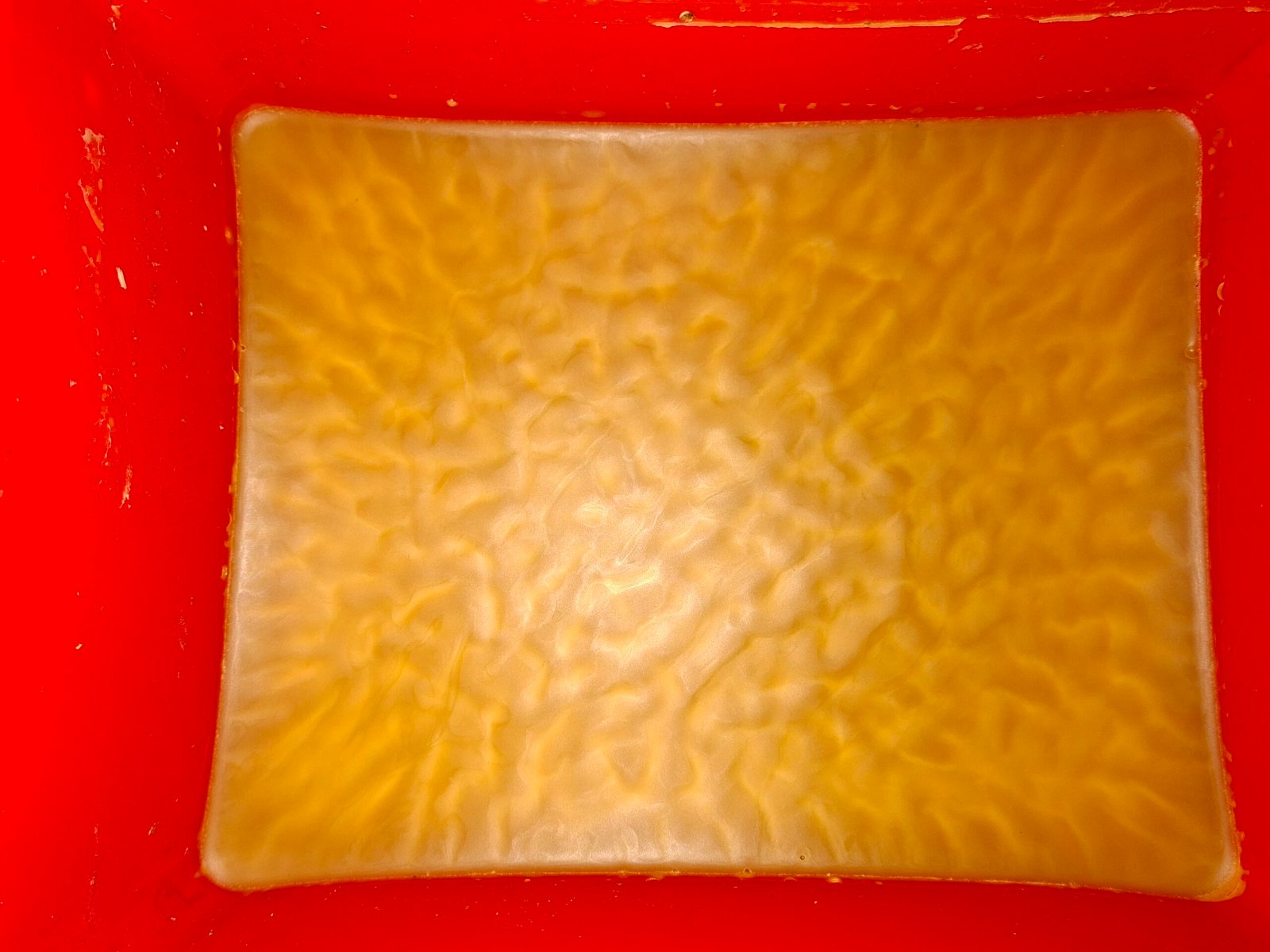 A set slab of pale gold filtered beeswax cooling in a mould, rippled surface