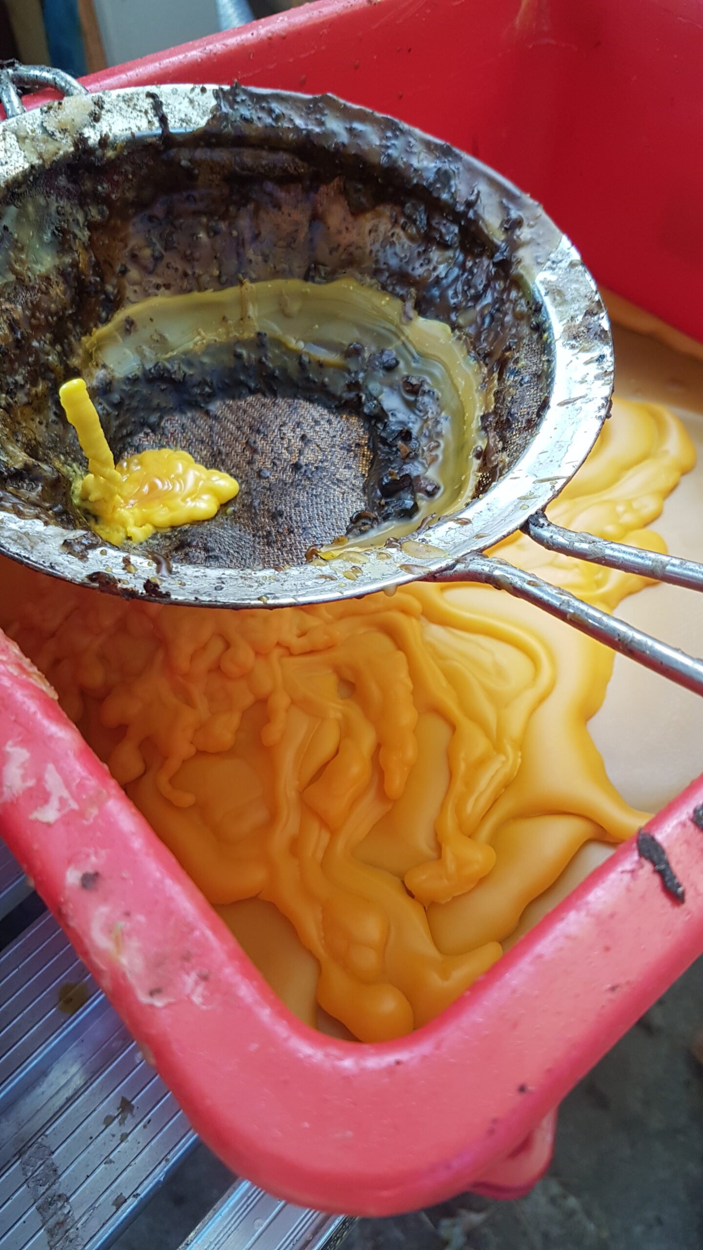 Molten beeswax being filtered through a metal sieve into a container