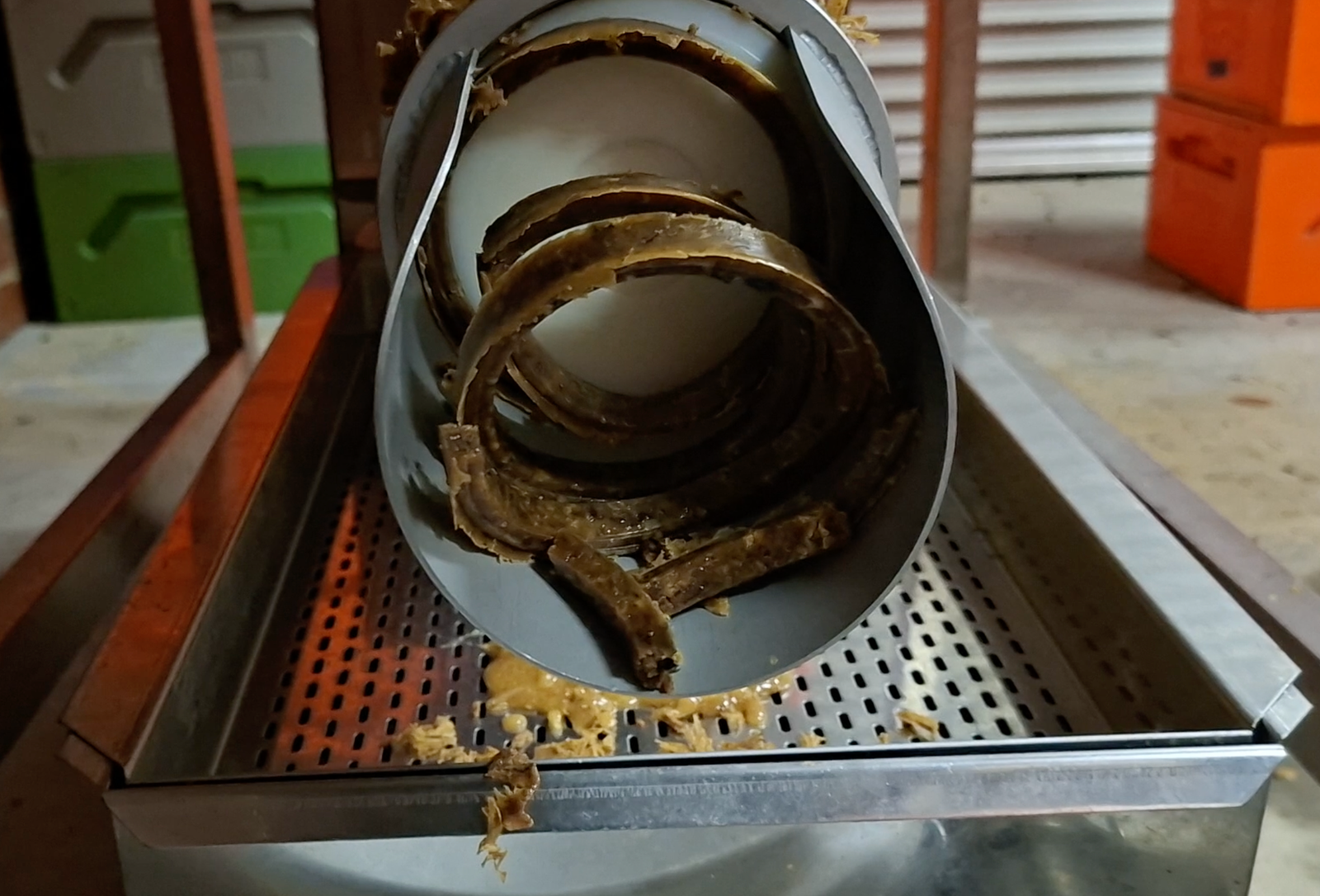 Cappings pressed through a stainless wax press, wax ribboning out and honey draining through the tray