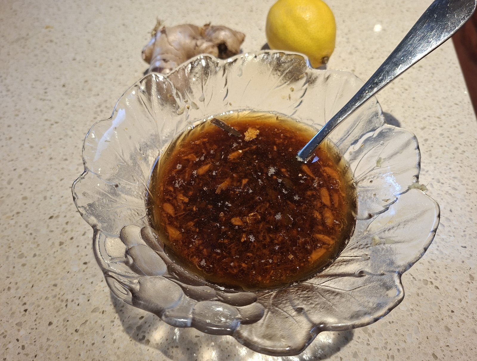 Honey soy marinade in a glass bowl with grated ginger and garlic, fresh ginger and a lemon behind