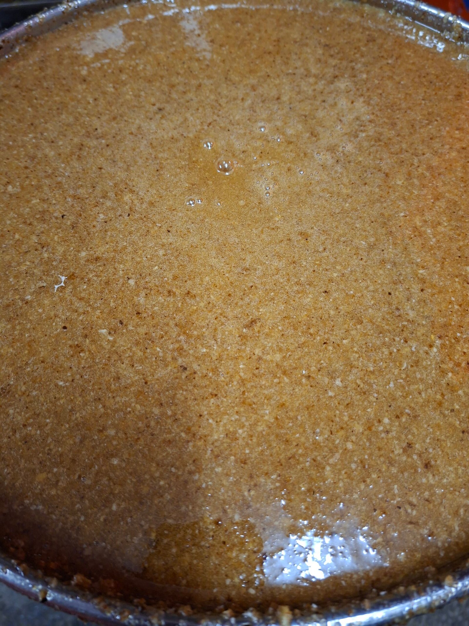 Raw unfiltered honey settling before the 400-micron sieve, its natural texture and fine pollen specks visible